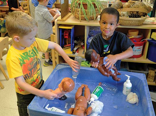 Two boys sharing a water table while they wash baby dolls